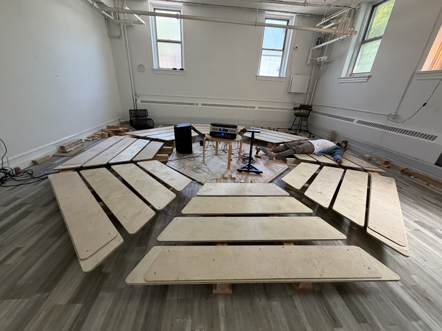 The SoundTemple listening room under construction in the basement of the School: listening beds arranged in a circle around audio gear, cables, and a builder lying on the floor.